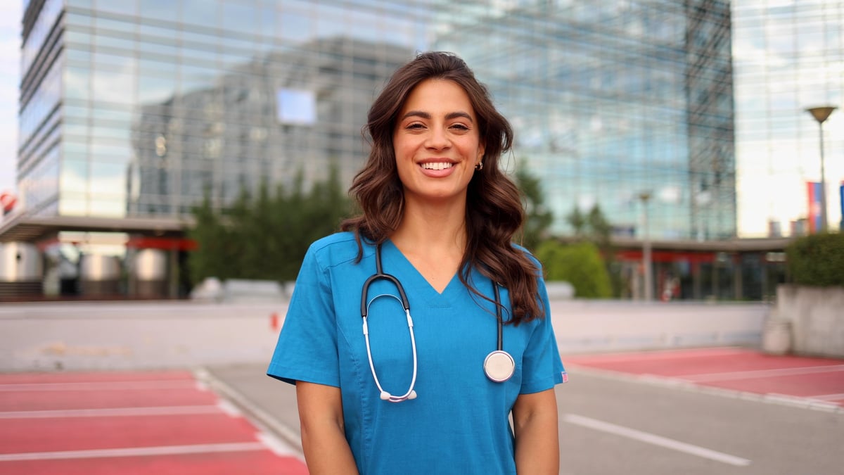 Médica sorrindo com jaleco branco em ambiente profissional de saúde, transmitindo confiança e acolhimento